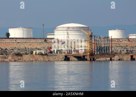 Lokale Bucht mit großen industriellen White Metal Ölraffinerie Tanks gefüllt und Laderampen umgeben von felsigen Ufer und ruhigen blauen Meer auf warmen sonnigen Stockfoto