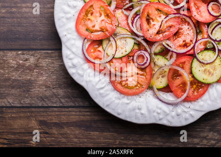 Eine frische, gesunde Salat mit Bio Tomaten, Gurken und Zwiebeln. Der Salat ist von oben gesehen. Es ist auf einem urigen braune Holztisch, in Th platziert Stockfoto