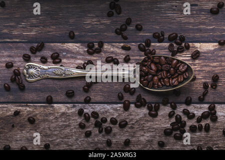 Eine alte Löffel mit Kaffeebohnen auf einem urigen braune Holztisch. Der Löffel ist voll mit Kaffeebohnen, und es gibt auch einige Kaffeebohnen auf verstreut Stockfoto