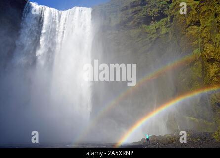 Mann steht unter doppelten Regenbogen am großen Wasserfall Skogafoss, Skogafoss, Skogar, Ring Road, Sudurland, South Island, Island Stockfoto