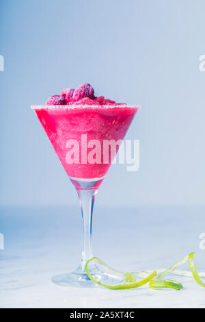 Eine frische Rosa gefrorene Himbeeren Drink in einem Zucker umrandet Martini Glas. Das Getränk wird mit gefrorenen Himbeeren und limettenschale Peel eingerichtet. Die backgrou Stockfoto