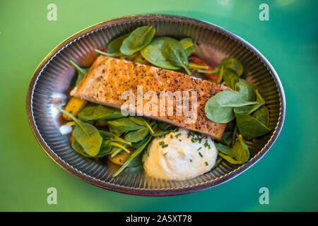 Eine gesunde Low Carb gegrillten Lachs, baby Spinatblätter und Joghurt Sauce in einem metallischen Schüssel. Grüner Hintergrund, von oben Perspektive. Stockfoto