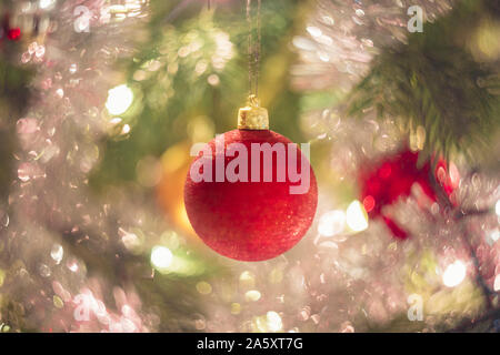 Close-up auf eine Zweigniederlassung, die in einem geschmückten Weihnachtsbaum. Eine rote Lampe ist im Fokus und es gibt defokussierten Glitzern und Leuchten im Baum. Stockfoto