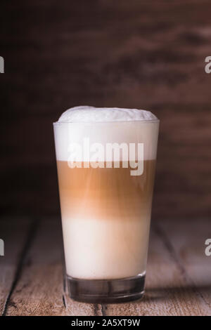 Kaffee Cafe Latte in einem hohen Glas auf einer hölzernen Hintergrund Macchiato. Es ist Kopieren Raum neben der Glas, und das Foto ist horizontal. Stockfoto