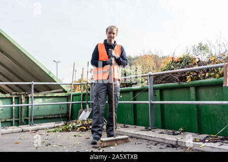 Mann, das Fegen des Fußbodens des Recycling Center nach der Bereitstellung von Abfällen grün Stockfoto