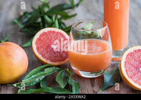 Ein Glas frische, gesunde organische Grapefruitsaft auf einem Holztisch. Es gibt eine Flasche des Grapefruitsaft im Hintergrund. Ein halbiert pink Grape Stockfoto