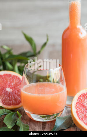 Ein Glas frische gesunde organische Grapefruit auf einem Holztisch. Es gibt eine Flasche des Grapefruitsaft im Hintergrund. Eine geschnittene rosa Grapefruit eine Stockfoto