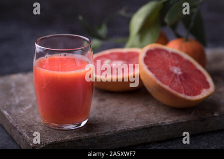 Gesunde organische Blut Orangensaft mit Blut Grapefruits und Orangen auf einem dunklen Stein Oberfläche. Dunkler Hintergrund, mit Defokussierten Obst verlässt. Stockfoto