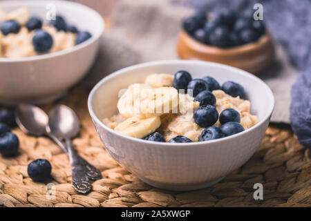 Gesundes Frühstück Haferflocken Porridge mit frischen Heidelbeeren und in Scheiben geschnittenen Bananen. Es gibt zwei Schüsseln auf dem Foto ist ein Teil aus dem Rahmen, und zwei v Stockfoto