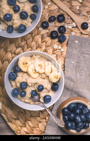 Gesundes Frühstück Haferflocken Porridge mit frischen Heidelbeeren und in Scheiben geschnittenen Bananen. Es gibt zwei Schüsseln auf dem Foto ist ein Teil aus dem Rahmen, und zwei v Stockfoto