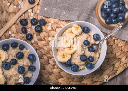 Gesundes Frühstück Haferflocken Porridge mit frischen Heidelbeeren und in Scheiben geschnittenen Bananen. Es gibt zwei Schüsseln auf dem Foto ist ein Teil aus dem Rahmen, und zwei v Stockfoto