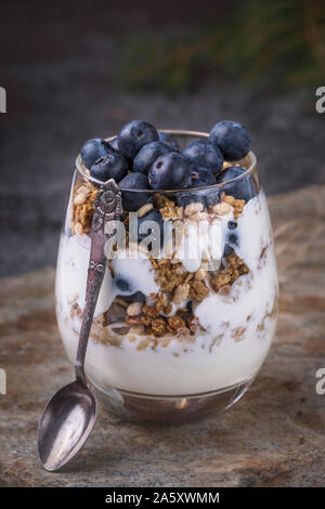 Ein frisches und gesundes Frühstück mit Joghurt, hausgemachtes Müsli und Blaubeeren in einem Glas. Das Glas ist auf einem abgenutzten Stein Oberfläche und neben das Glas ist ein Stockfoto