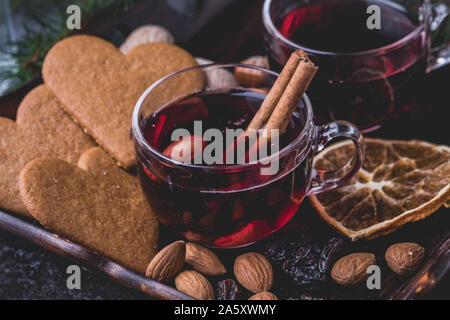 Glühwein Mit Zimtstangen. Die Gläser sind auf einem dunklen Holz- fach umgeben von Herzförmige traditionelle schwedische Lebkuchen cookies, Rosinen, al Stockfoto