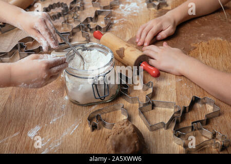 Die Hände und Arme von zwei Kinder backen schwedische Lebkuchen cookies mit verschiedenen Spaß cutter Formen. Auf dem hölzernen Eiche Tisch mit den Formen und Teig Stockfoto