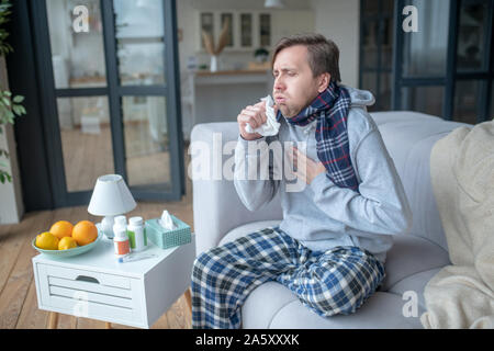 Mann sitzt auf einem Sofa und Husten nach Einnahme von Vitaminen Stockfoto