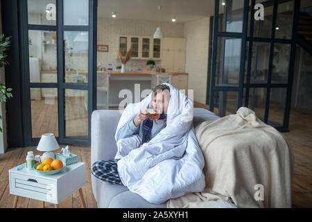 Man Frieren so trinken heißen Tee und Decke im bettlaken Stockfoto