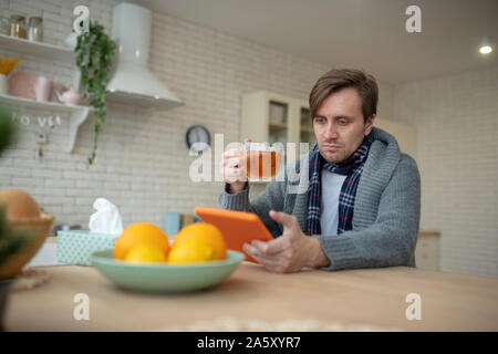 Dunkelhaarigen Mann news Lesen auf Tablet und Tee trinken. Stockfoto