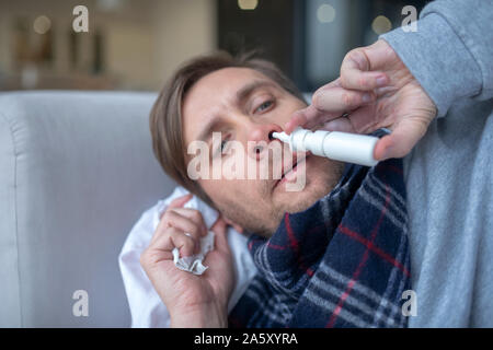 Blauäugiger Mensch, verstopfte Nase Nasenspray nehmen Stockfoto