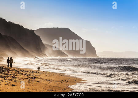 Zwei Frauen gehen ihren Hund auf Charmouth Beach bei Sonnenaufgang. Stockfoto