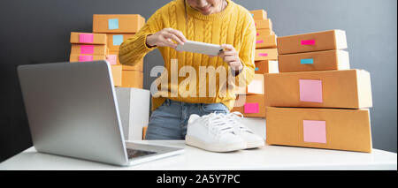 Junge Frauen, die foto Schuhe mit Mobiltelefon oder Smartphone digitale Kamera für Post und online über das Internet zu verkaufen und Vorbereitung Pack Produkt Stockfoto
