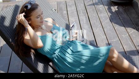 Frau im blauen Kleid in Lounge Chair mit Smartphone Stockfoto