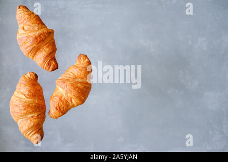 Drei frisch gebackene Croissants Fliegen auf grauem Hintergrund. Für Text platzieren. Kreative Bäckerei Konzept Stockfoto