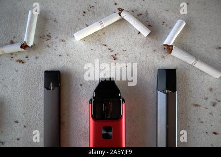 Verschiedene vape Geräte elektronische Zigaretten rauchen als Alternativen mit gebrochenen Zigaretten und Tabak verstreut auf weiße strukturierte Hintergrund schließen u Stockfoto