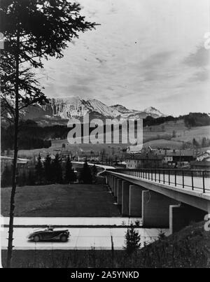 Auto nähern Überführung auf der Autobahn (Autobahn) mit Blick auf die Landschaft und die Berge im Hintergrund. zwischen 1936 und 1939 datiert. Stockfoto