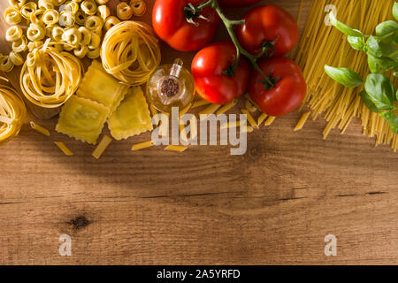 Italienische Pasta und Zutaten. Ravioli, Nudeln, Spaghetti, Tortellini, Tomaten und Basilikum auf hölzernen Tisch Stockfoto