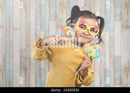 Süße kleine asiatische Mädchen halten und essen eine bunte Lollipop. Konzept der Mundpflege und Süßigkeiten Tag Stockfoto