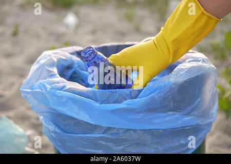 Bewusste junge Freiwillige in gelbe Gummihandschuhe ist Laufen mit Müllsack entlang einer grünen Zone eines schmutzigen Küste des Flusses und Reinigung, Abfall, Stockfoto