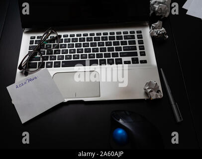 Verschiedene Objekte auf schwarz Büro Schreibtisch. Moderne schwarze Büro Schreibtisch Tisch mit Laptop Tastatur, Maus, Stift, zerknittertes Papier Kugeln, Gläser, Kurznotiz wi Stockfoto