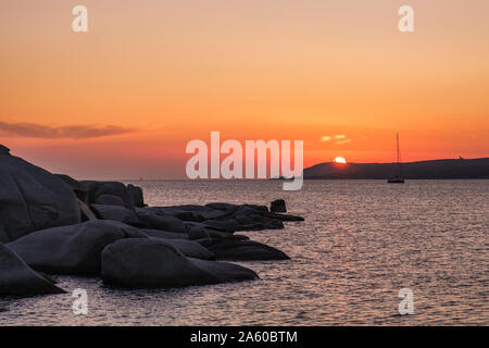 Yacht günstig in einer Bucht, wie die Sonne über dem Mittelmeer und große Granitblöcke, die an der Küste von Cavallo Insel im Archipel Lavezzi setzt Stockfoto