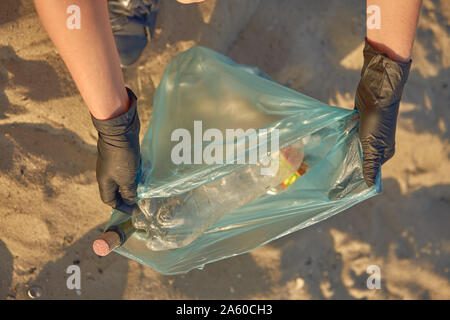 Verantwortliche Person im schwarzen Handschuhen ist Laufen mit Müllsack entlang einer schmutzigen Strand des Flusses und Reinigung, Abfall. Die Menschen und der Ökologie. Küste pollu Stockfoto