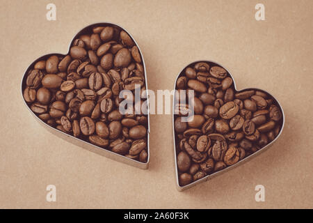 Zwei Herzen von Kaffeebohnen auf braunem Hintergrund. Handwerk Papier. Art Design. Vintage Pergament. Form des Herzens, Symbol der Liebe. Heap Röstkaffee bea Stockfoto