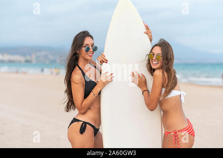 Zwei glückliche weibliche Freunde mit Surfbrett am Strand Stockfoto