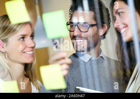 Drei Lächeln Geschäftsleute gemeinsam Brainstorming mit Haftnotizen auf eine Glaswand Stockfoto