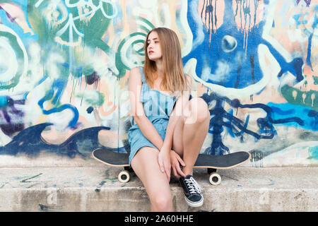 Junge Frau sitzt auf Skateboard vor Graffiti Stockfoto