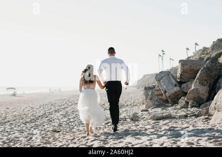 Rückansicht der Braut und des Bräutigams, die auf den Strand Stockfoto