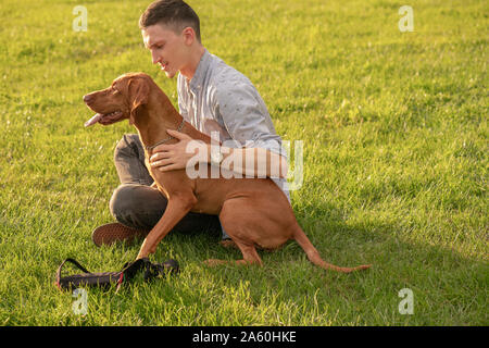 Junger Mann mit seinem Hund, kuscheln auf einer Wiese Stockfoto