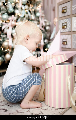 Kleinkind Eröffnung Geschenkbox vor Weihnachtsbaum Stockfoto