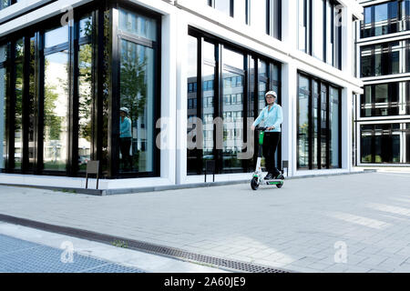 Reife Frau reiten Elektroroller in der Stadt Stockfoto