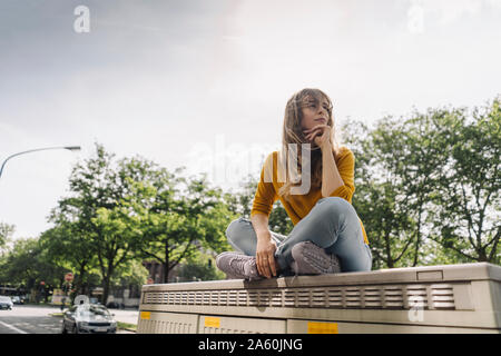Junge Frau sitzt auf einem Feld in der Stadt Stockfoto