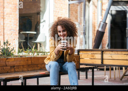 Portrait Of Smiling teenage Mädchen sitzt auf der Bank mit Kaffee zu gehen Stockfoto