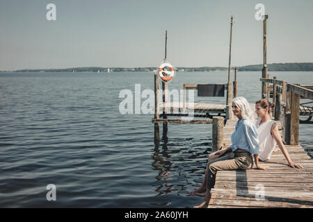 Mutter und Tochter sitzen am Bootsanleger, Entspannen am Meer Stockfoto