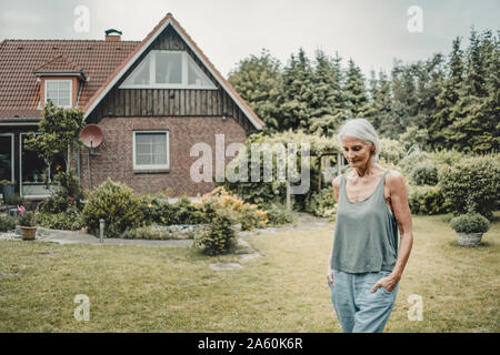 Ältere Frau zu ihrem Garten, mit den Händen in den Taschen Stockfoto