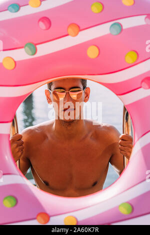 Portrait der junge Mann hinter aufblasbarer Schwimmer in Donut Form Stockfoto