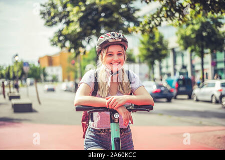 Porträt der jungen Frau mit radhelm am Lenker der E-Scooter, Berlin, Deutschland lehnte sich entspannt Stockfoto