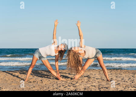 Zwei Frauen praticing Acro Yoga am Strand, Dreieck darstellen Stockfoto