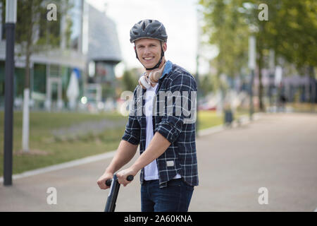 Portrait von lächelnden jungen Mann mit e-Scooter in der Stadt Stockfoto